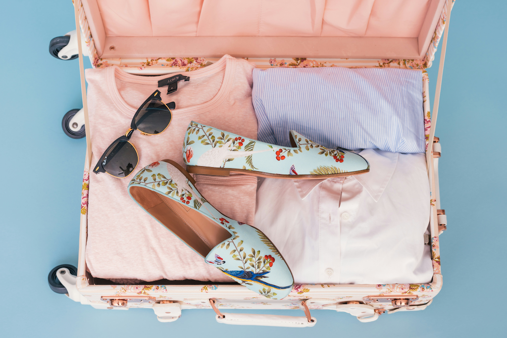 Ein gepackter Koffer mit Hemden, Sonnenbrille und Schuhen